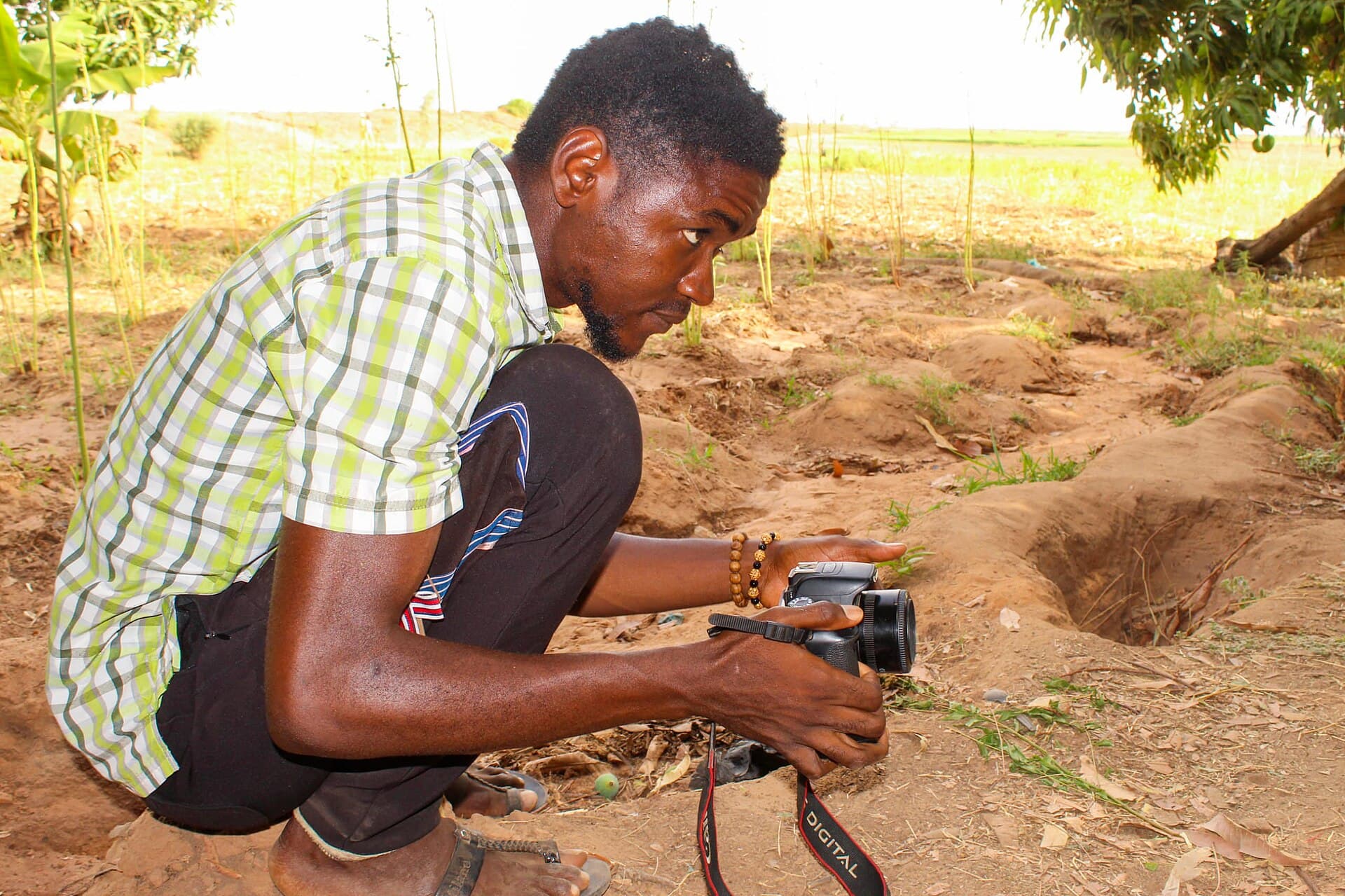 A man crouching in a field, photographing something on the ground